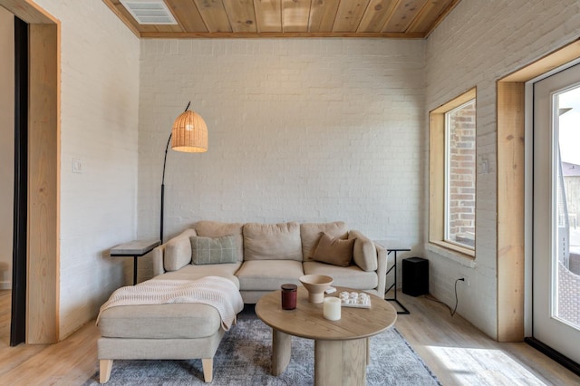 living room featuring wood ceiling, plenty of natural light, light hardwood / wood-style floors, and brick wall