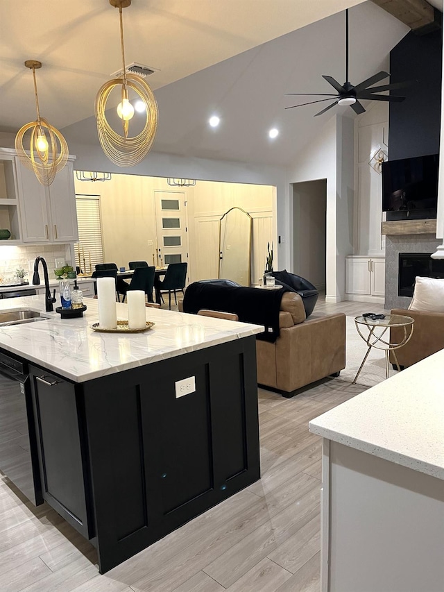 kitchen featuring pendant lighting, dishwasher, white cabinetry, sink, and light stone countertops