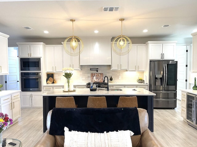 kitchen featuring wine cooler, white cabinetry, hanging light fixtures, appliances with stainless steel finishes, and a kitchen island with sink