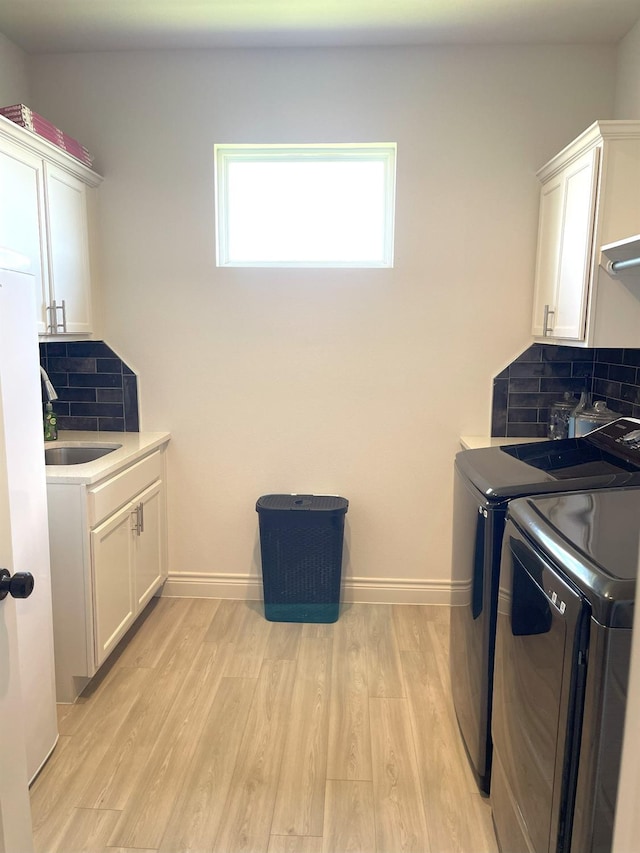 clothes washing area featuring cabinets, sink, washing machine and clothes dryer, and light hardwood / wood-style floors