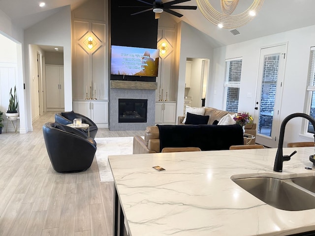 kitchen featuring vaulted ceiling, sink, light stone counters, and light hardwood / wood-style floors