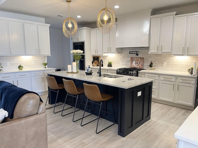 kitchen with white cabinetry, sink, decorative light fixtures, and a kitchen island with sink