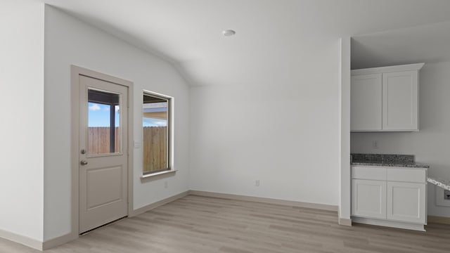 unfurnished dining area featuring light wood finished floors, vaulted ceiling, and baseboards