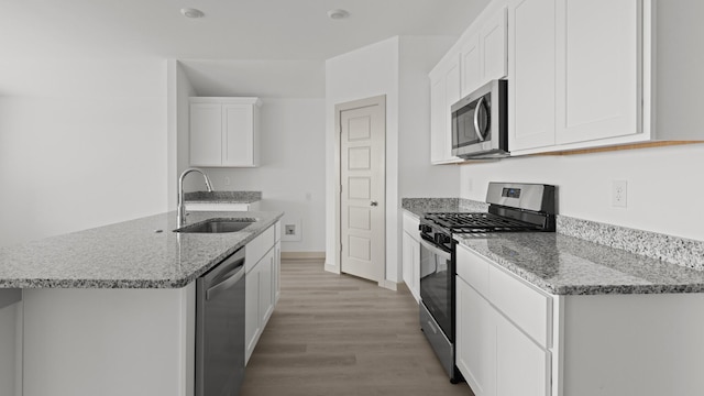 kitchen featuring light wood finished floors, a sink, white cabinetry, light stone counters, and appliances with stainless steel finishes