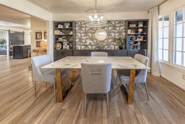 dining area with a healthy amount of sunlight, a barn door, a chandelier, and light hardwood / wood-style floors