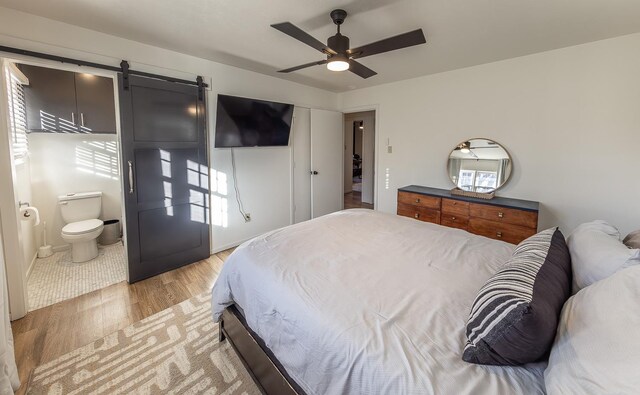 bedroom with ensuite bath, light hardwood / wood-style floors, a barn door, and ceiling fan