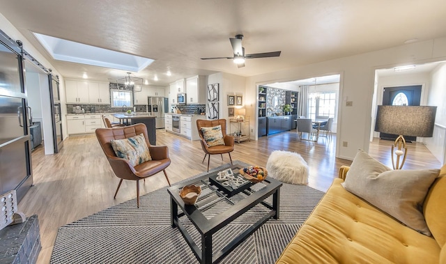 living room with ceiling fan with notable chandelier, sink, and light hardwood / wood-style floors