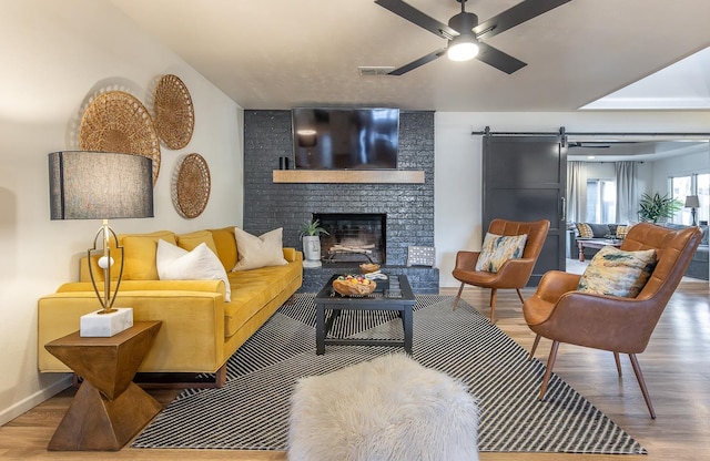 living room with ceiling fan, a barn door, hardwood / wood-style floors, and a fireplace