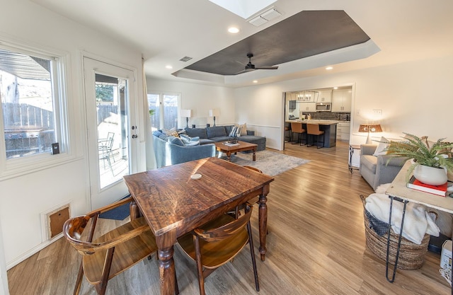 dining area featuring a skylight, a tray ceiling, light hardwood / wood-style flooring, and ceiling fan