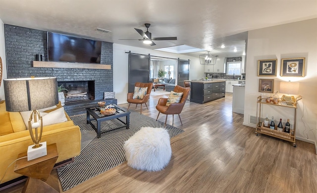 living room featuring a barn door, hardwood / wood-style floors, a fireplace, and ceiling fan