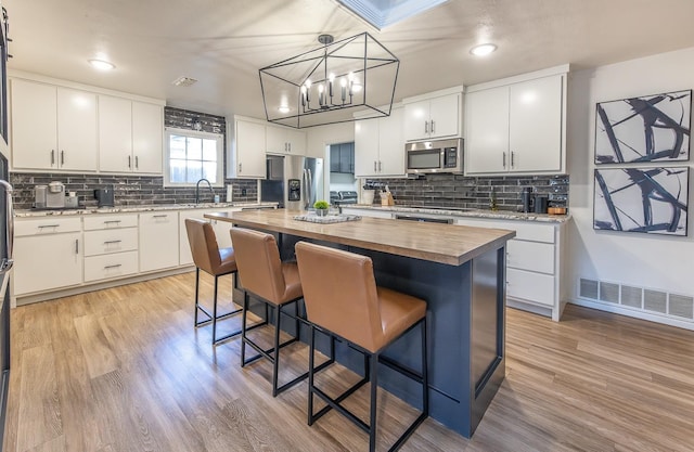 kitchen with a kitchen island, wood counters, a breakfast bar area, white cabinets, and stainless steel appliances