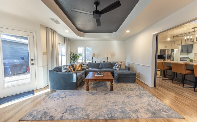 living room with ceiling fan, a raised ceiling, and light wood-type flooring