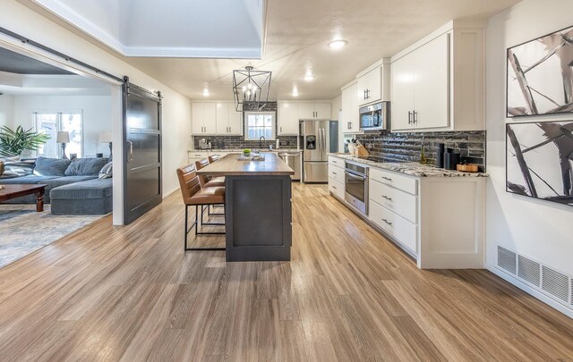 kitchen featuring pendant lighting, appliances with stainless steel finishes, white cabinetry, a kitchen island, and a barn door