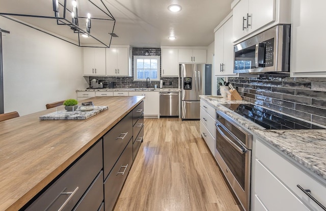 kitchen with appliances with stainless steel finishes, decorative light fixtures, butcher block counters, white cabinets, and light wood-type flooring