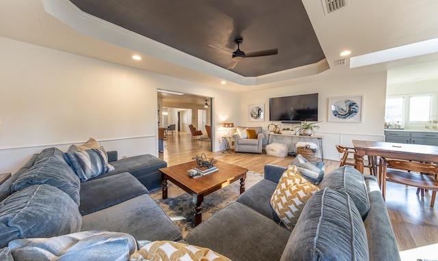 living room with a raised ceiling, ceiling fan, and light hardwood / wood-style flooring