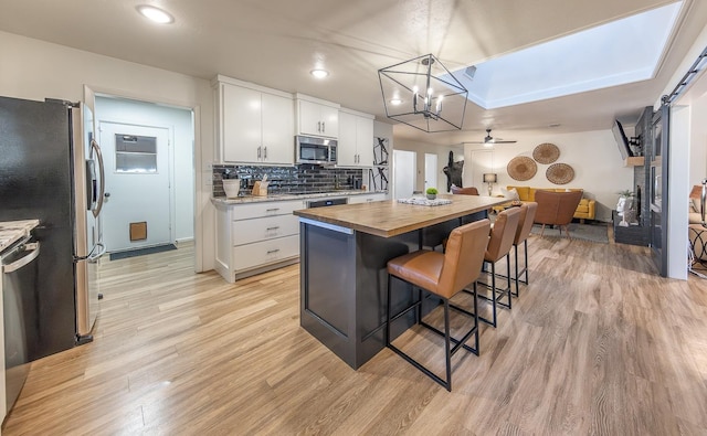 kitchen featuring a kitchen island, appliances with stainless steel finishes, butcher block countertops, decorative light fixtures, and white cabinets