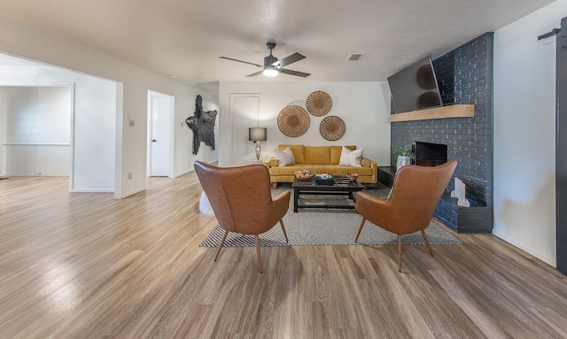 living room with ceiling fan, a barn door, a fireplace, and light wood-type flooring