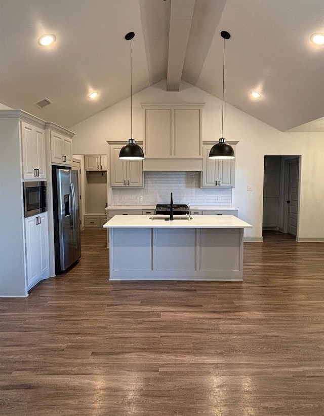 kitchen with stainless steel refrigerator with ice dispenser, built in microwave, sink, hanging light fixtures, and a center island with sink