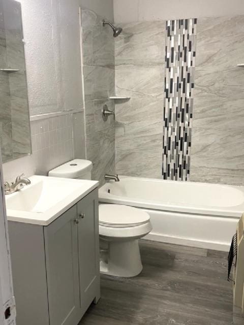 full bathroom with tile walls, vanity, wood-type flooring, tiled shower / bath, and toilet