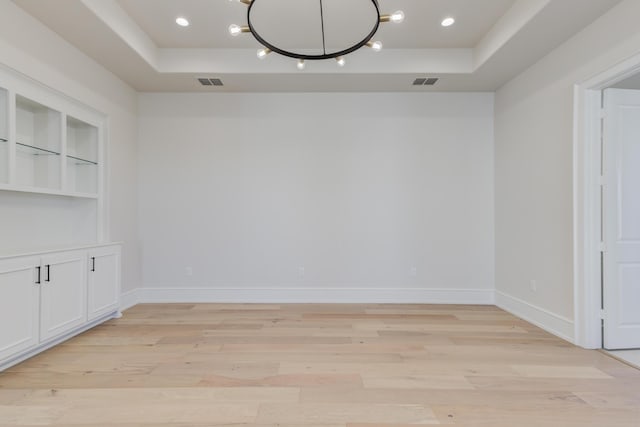 interior space with a raised ceiling, light wood-type flooring, and visible vents