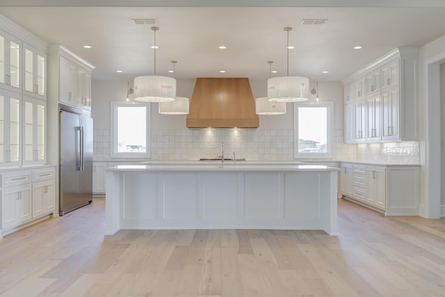 kitchen featuring custom exhaust hood, light countertops, high quality fridge, and white cabinets