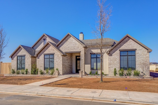 view of front of home with a shingled roof, brick siding, fence, and a chimney