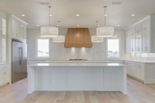 kitchen featuring visible vents, high quality fridge, premium range hood, and light countertops