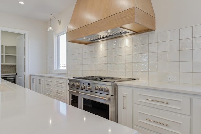kitchen with white cabinets, double oven range, custom exhaust hood, light countertops, and decorative backsplash