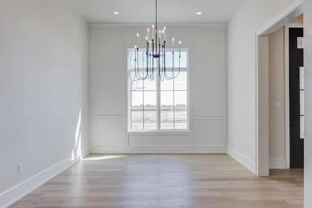unfurnished dining area featuring a decorative wall, light wood finished floors, plenty of natural light, and a notable chandelier