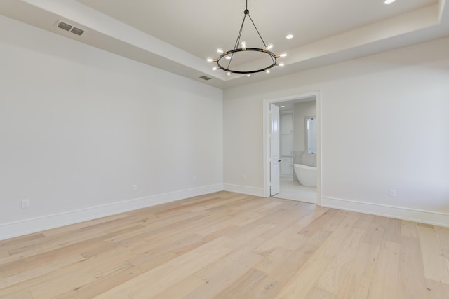 empty room featuring light wood-type flooring, a raised ceiling, an inviting chandelier, and baseboards