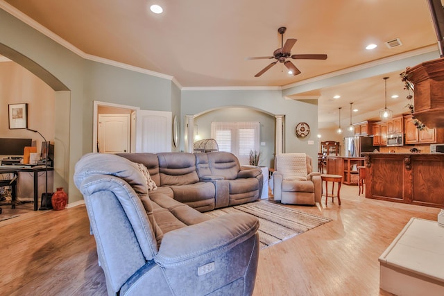 living room featuring light wood-style floors, visible vents, arched walkways, and crown molding