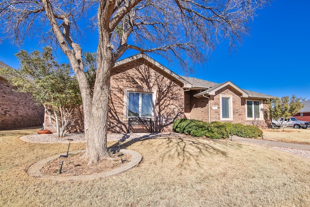 single story home featuring roof with shingles, a front lawn, and brick siding