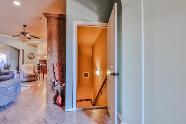 hallway featuring arched walkways, wood finished floors, visible vents, an upstairs landing, and ornate columns