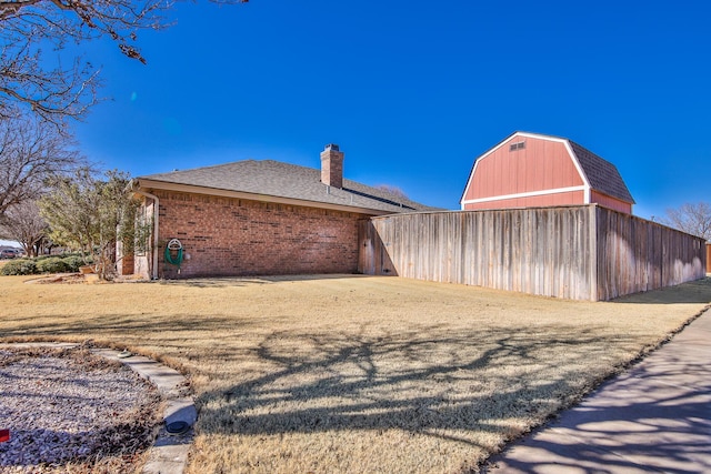 view of property exterior featuring brick siding, a chimney, a shingled roof, a barn, and an outdoor structure