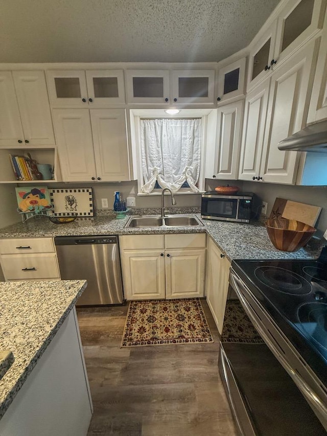 kitchen featuring sink, dark wood-type flooring, stainless steel appliances, light stone countertops, and a textured ceiling