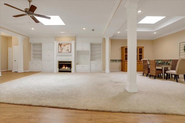 carpeted living room with ornate columns, crown molding, and a skylight