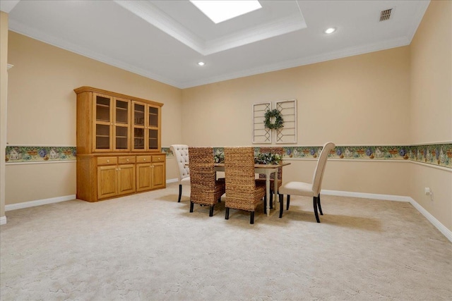 carpeted dining room with a raised ceiling, ornamental molding, and a skylight