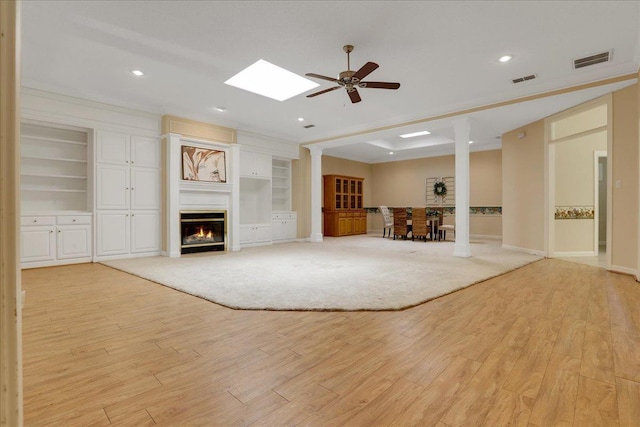 unfurnished living room with a skylight, light wood-type flooring, ornamental molding, built in features, and ceiling fan