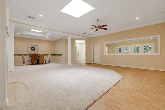 living room featuring a skylight, light hardwood / wood-style flooring, ornamental molding, a raised ceiling, and ceiling fan