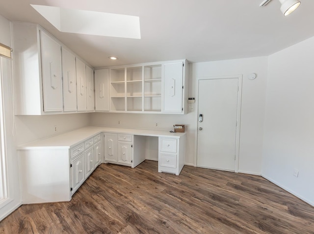 unfurnished office featuring a skylight, dark hardwood / wood-style floors, and built in desk