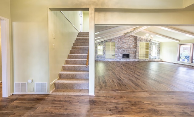 unfurnished living room with a notable chandelier, a stone fireplace, wood-type flooring, and lofted ceiling with beams