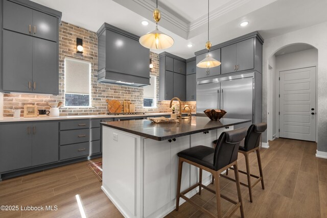 4606 138th Pl, Lubbock, TX 79424 - kitchen with wall chimney exhaust hood, gray cabinets, arched walkways, wood finished floors, and decorative backsplash