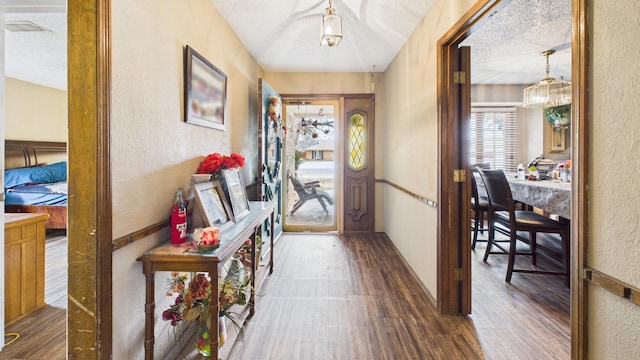 hall with wood finished floors, a textured wall, and a textured ceiling