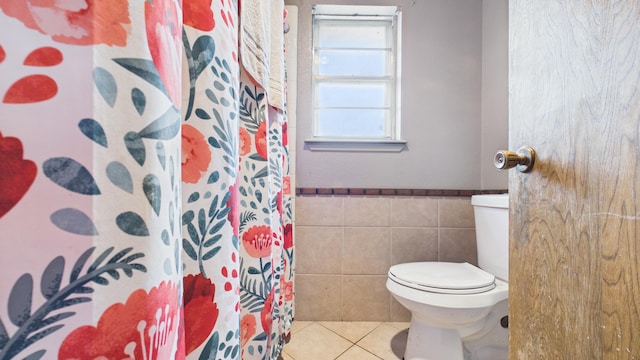 bathroom featuring tile patterned floors, tile walls, a shower with shower curtain, a wainscoted wall, and toilet