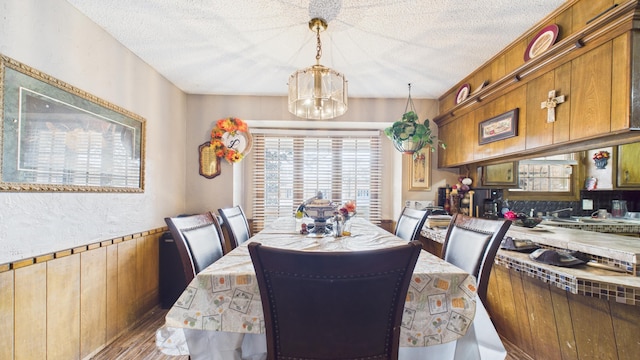 dining area with wood walls, wood finished floors, an inviting chandelier, and a textured ceiling