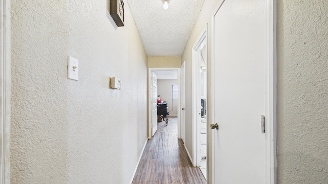corridor with baseboards, wood finished floors, a textured ceiling, and a textured wall