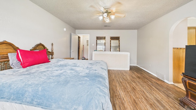 bedroom with ceiling fan, visible vents, a textured ceiling, arched walkways, and wood finished floors