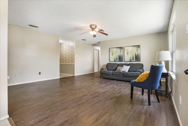 living room featuring dark wood-type flooring, ceiling fan, and a textured ceiling