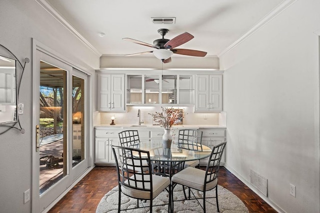 dining room with ornamental molding, sink, ceiling fan, and dark parquet floors