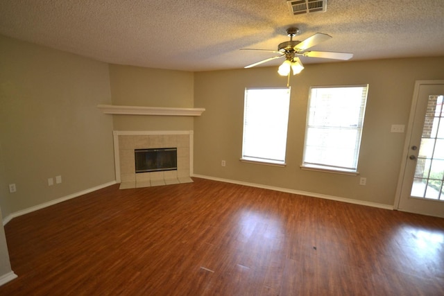 unfurnished living room featuring a tiled fireplace, ceiling fan, a textured ceiling, and dark hardwood / wood-style flooring